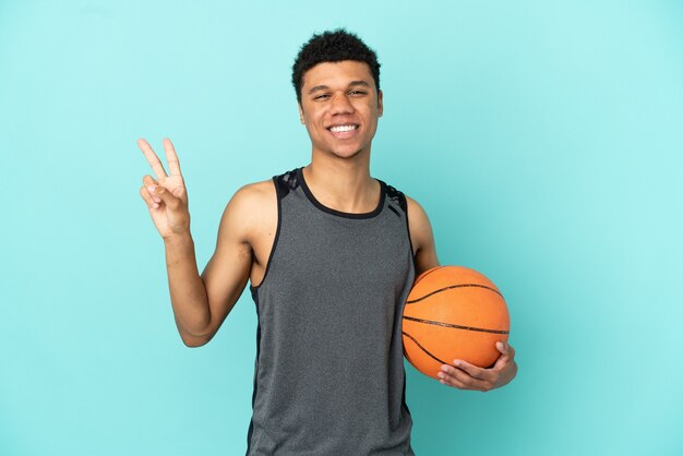 Joueur de basket-ball homme afro-américain isolé sur fond bleu souriant et montrant le signe de la victoire