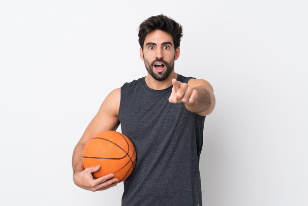 Joueur de basket-ball homme avec barbe sur mur blanc isolé surpris et pointant vers l'avant