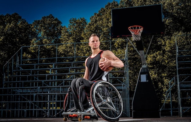 Un joueur de basket-ball infirme en fauteuil roulant tient une balle sur un terrain de jeu ouvert.