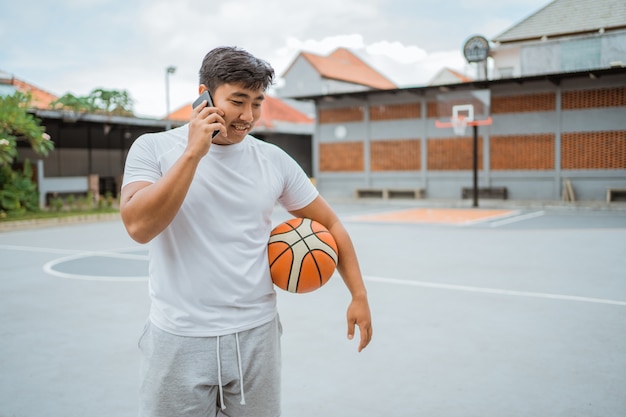 Un joueur de basket-ball passe un appel téléphonique en tenant le ballon debout