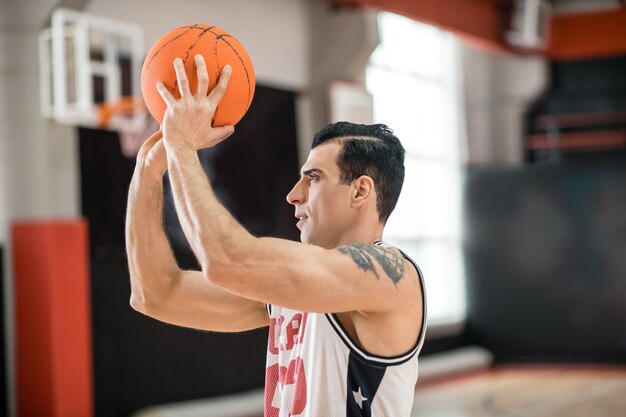 Joueur de basketball. Jeune homme avec tatoo lançant une balle dans un anneau