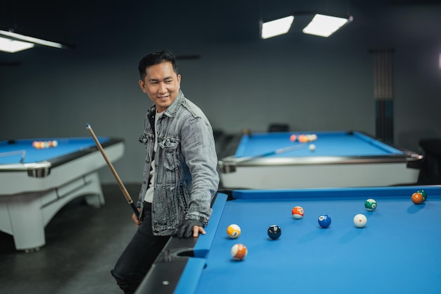 Le joueur de billard masculin souriant à la caméra en se tenant debout et posant ses mains sur la piscine