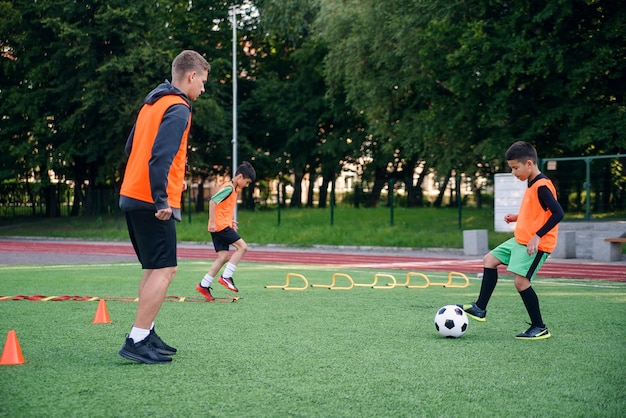 Joueur enfant en uniforme de football travaillant sur le ballon avec l'entraîneur