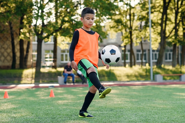 Un joueur de football adolescent motivé fourre un ballon de football sur ses pieds avec des bottes