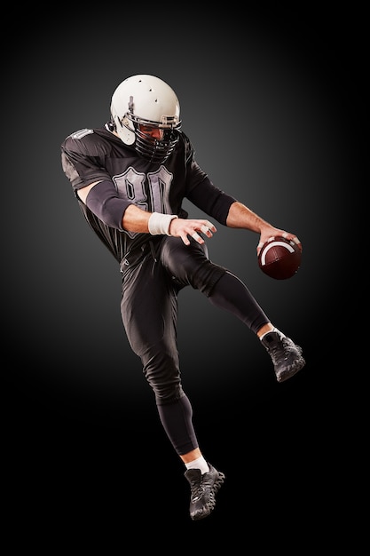 Joueur de football américain en uniforme sombre saute avec le ballon sur une surface noire