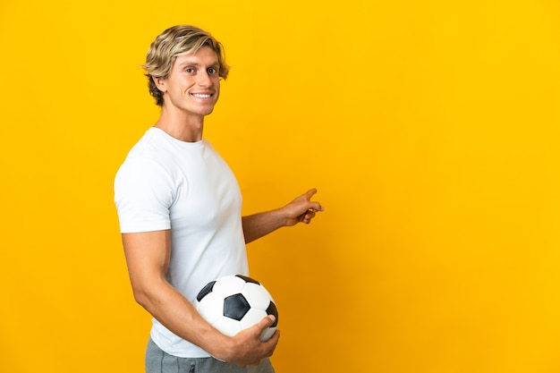 Joueur de football anglais sur mur jaune isolé pointant vers l'arrière