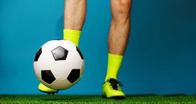 Photo joueur de football avec ballon sur l'herbe verte et fond bleu