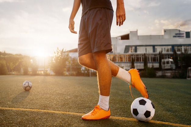 Joueur de football avec ballon sur le terrain au lever du soleil. Footballeur sur stade extérieur, entraînement avant le match, entraînement de football