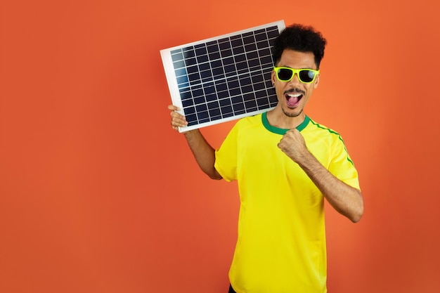Joueur de football Black Man Celebrating Holding panneau solaire photovoltaïque isolé sur fond orange
