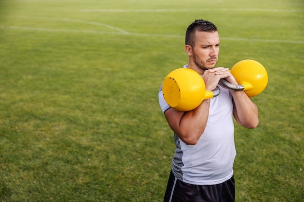 Photo joueur de football mal rasé attrayant en forme faisant de l'endurance avec des cloches de bouilloire.