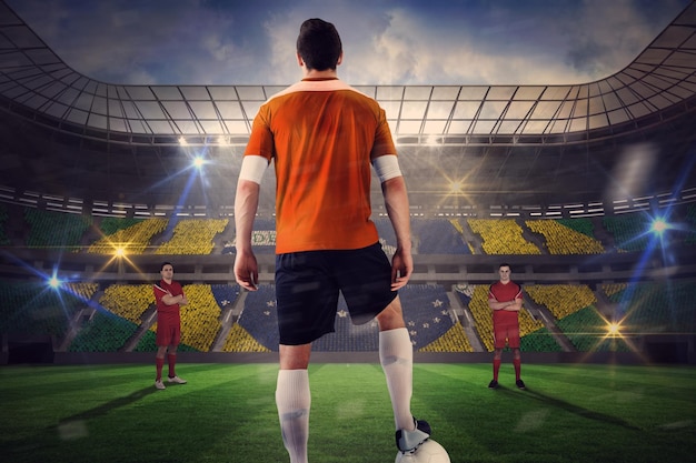 Joueur de football en orange avec ballon face à l'opposition contre un grand stade de football avec des fans brésiliens