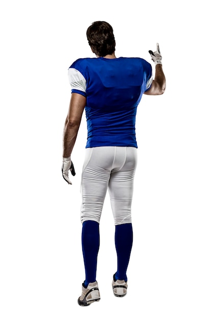 Joueur de football avec un uniforme bleu marchant, montrant son dos sur un mur blanc