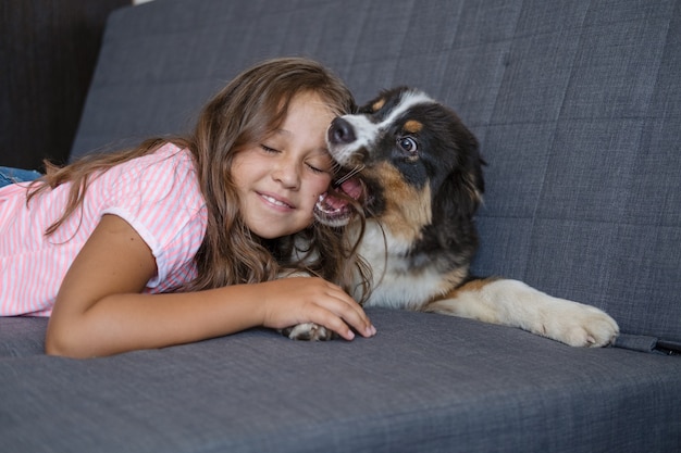 Joueur heureux berger australien chiot trois couleurs chien couché jouer avec propriétaire jolie fille caucasienne d'âge élémentaire.