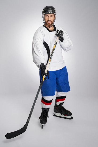 Joueur de hockey sur glace souriant avec bâton et casque de protection posant en studio vue de face de beau