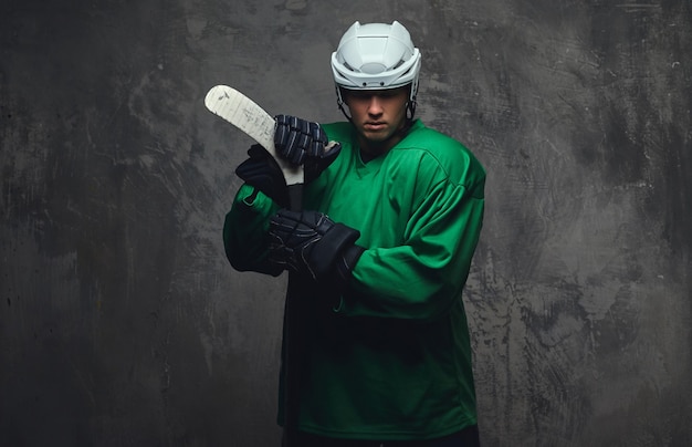 Joueur de hockey portant un équipement de protection vert et un casque blanc debout avec le bâton de hockey. Isolé sur un fond gris.