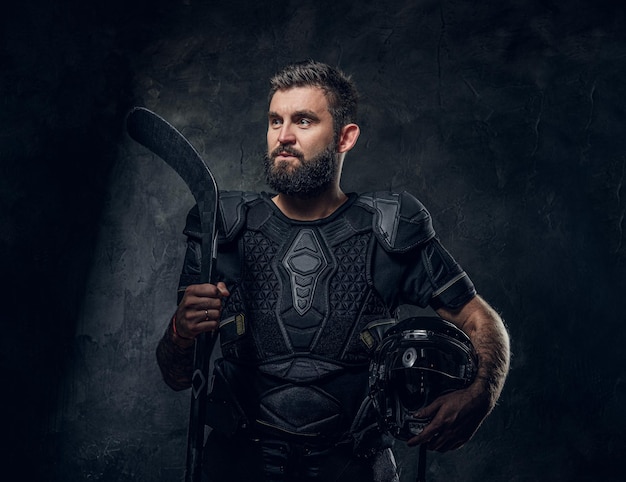 Un joueur de hockey tatoué brutal pose pour un photographe dans un studio photo sombre.