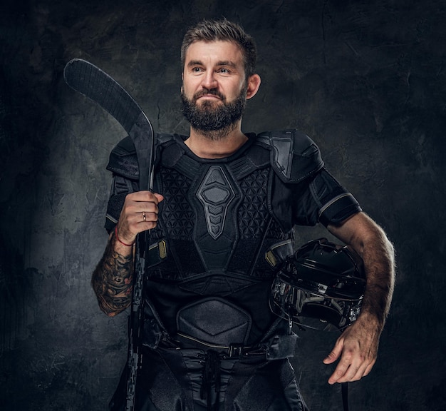 Un joueur de hockey tatoué brutal pose pour un photographe dans un studio photo sombre.