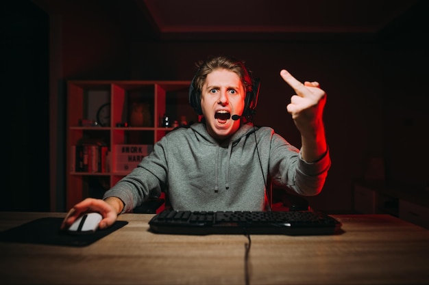 Un joueur insatisfait émotionnel dans un casque regarde avec colère la caméra tout en jouant sur l'ordinateur