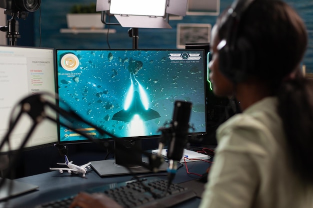 Joueur professionnel afro-américain portant un casque parlant avec des joueurs distants pendant la diffusion en direct à l'aide de microphones de jeu. Joueur concentré jouant à des jeux vidéo de tir spatial pendant le championnat en ligne