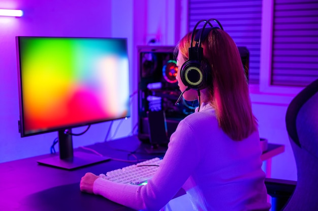 Un joueur professionnel asiatique jouant à un jeu vidéo en ligne sur un ordinateur de bureau a des lumières LED au néon colorées dans une pièce sombre jeune femme dans un casque de jeu utilisant un ordinateur pour jouer à un jeu à la maison Vue arrière