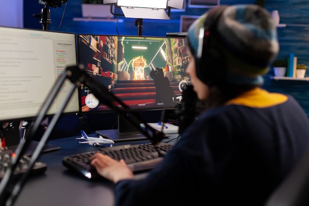 Joueur professionnel assis sur une chaise de jeu au bureau et parlant dans un microphone pour la compétition de jeux vidéo de tir spatial. Femme diffusant des jeux vidéo en ligne pour un tournoi esport dans une salle avec des néons