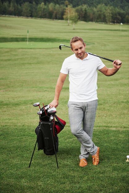 Un joueur professionnel se tient sur un terrain de golf, tient un sac en métal et un sac de golf