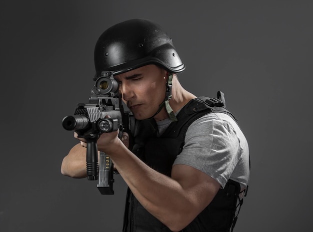 joueur de sport de paintball portant un casque de protection visant un pistolet, une armure noire et une mitrailleuse