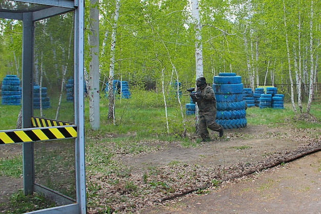 Joueur de sport de paintball portant un masque de protection visant une arme à feu depuis un abri sous une attaque par balle