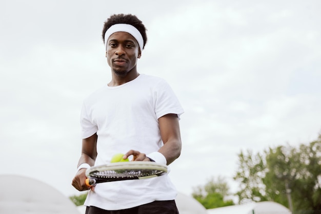 Un joueur de tennis d'apparence africaine se tient sur un court de tennis tenant une raquette