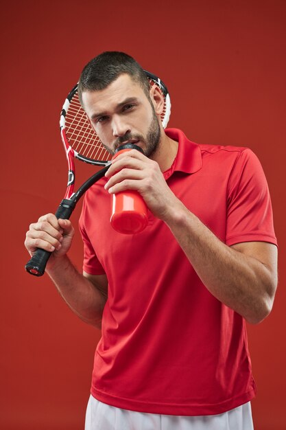 Joueur de tennis aux cheveux noirs posant devant l'appareil photo avec un outil de sport dans les mains isolées