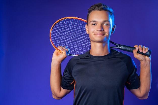 Joueur de tennis caucasien jeune homme posant avec une raquette de tennis sur fond violet close up