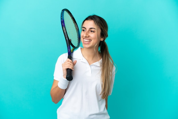 Joueur de tennis de jeune femme isolé sur fond bleu regardant sur le côté et souriant