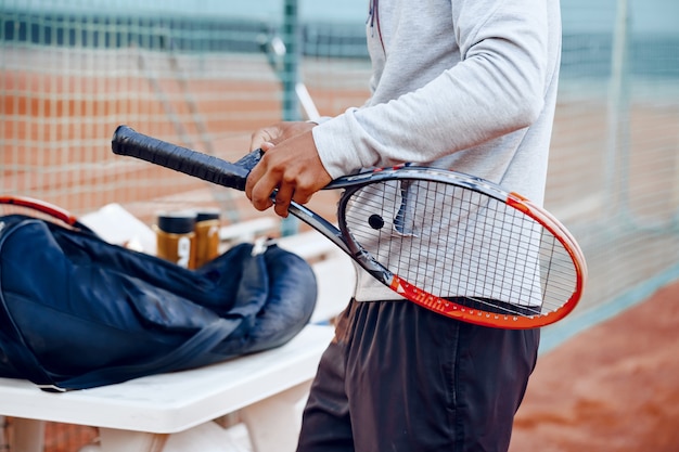 Un joueur de tennis méconnaissable répare la couverture de la poignée de la raquette de tennis