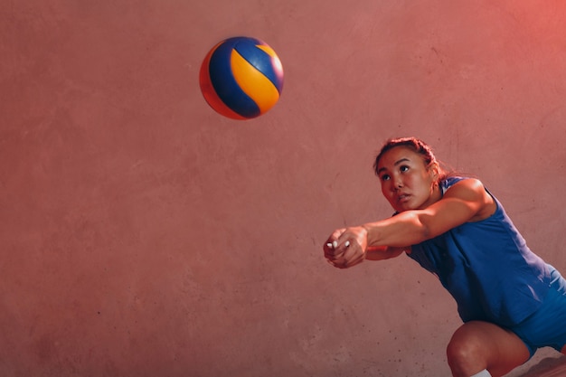 Joueur de volley-ball de jeune femme asiatique en uniforme bleu avec ballon