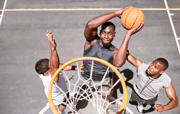 Joueurs de basket-ball empêchant un joueur de plonger une balle dans le filet pour marquer des points lors d'un match sur un terrain de sport d'en haut Athlètes en forme sautant pour défendre dans un jeu de compétition pour le plaisir récréatif