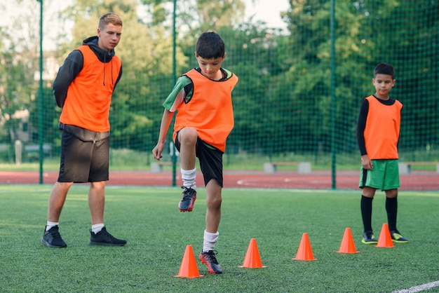 Les joueurs de football qui courent entre les cônes orange en plastique sur le stade artificiel