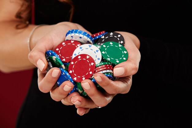 Une joueuse de poker avec des ongles blancs peints tient ses jetons de poker pour faire un pari. Concept d'entreprise de jeu et de casino