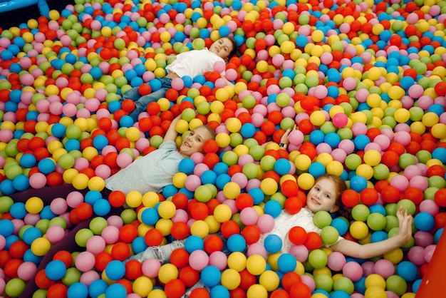 Jouful enfants allongés parmi de nombreuses boules colorées dans le centre de divertissement. Loisirs filles et garçons en vacances, bonheur de l'enfance, enfants heureux sur l'aire de jeux