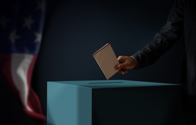 Jour de l'élection aux États-Unis d'Amérique Concept. Personne déposant une carte de vote dans l'urne. Drapeau USA accroché au mur. Ton sombre cinématographique