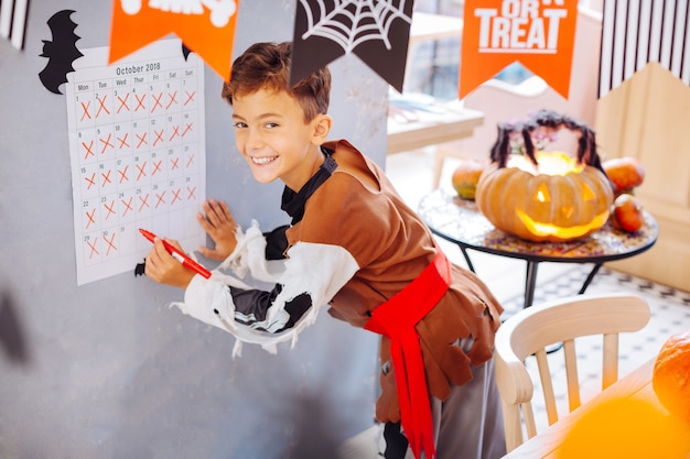 Jour de fête. Rayonnant beau garçon vêtu d'un costume d'Halloween se sentant extrêmement heureux le jour de la célébration