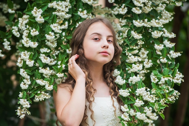 Ce jour-là printemps floraison arbre été nature femme coiffeur mode petite fille aux longs cheveux bouclés petite beauté en robe blanche mariage ange enfant enfant profiter de la fleur de jasmin dans le parc