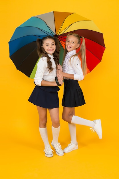 Jour de pluie. Enfance heureuse. Temps scolaire. Parapluie arc-en-ciel. Vie colorée. Écolières heureux grand parapluie. Prévisions météorologiques d'automne. Place pour nous deux. Accessoire de mode. Amies filles avec parapluie.