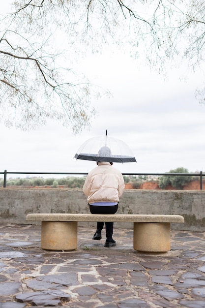 Jour de pluie Fille avec un parapluie transparent assis sur un banc sous la pluie