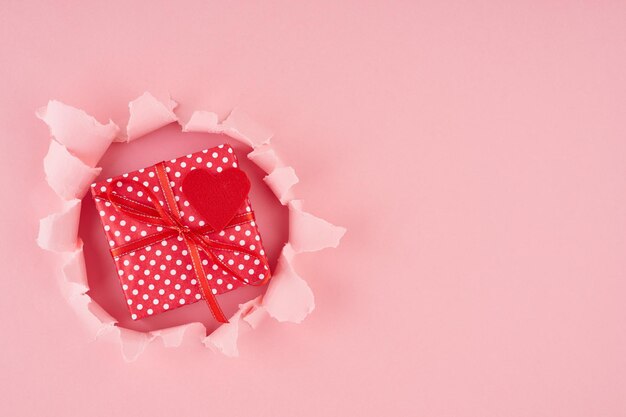 Photo jour de la saint-valentin un trou déchiré et un cœur rouge avec une boîte cadeau en rose vif