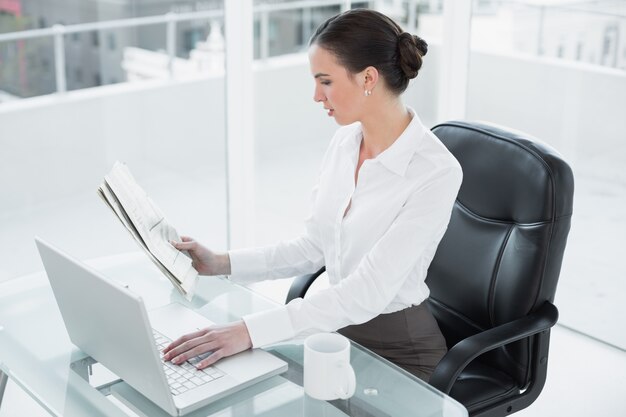 Journal de lecture de femme d&#39;affaires et d&#39;utiliser un ordinateur portable au bureau