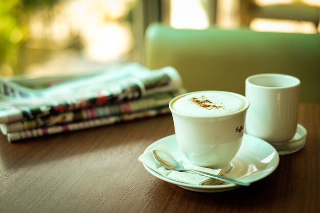 Journal et tasse de café chaud (cappuccino) décoré de café en poudre et de lait