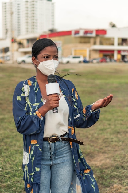 Une journaliste africaine en masque parlant au microphone dans la rue de la ville