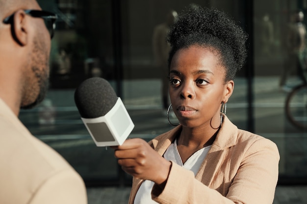 Journaliste africaine tenant un microphone et interviewant l'homme à l'extérieur