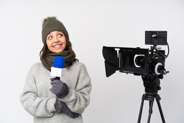 Journaliste femme tenant un microphone et rapportant des nouvelles sur un mur blanc isolé en levant tout en souriant