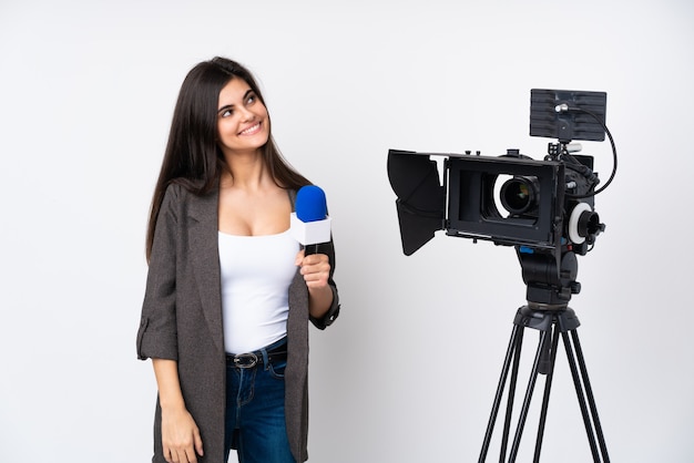 Journaliste femme tenant un microphone et rapportant des nouvelles sur le mur blanc en riant et en levant